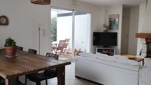 Zona de menjador amb taula i cadires de fusta, una planta en test i un televisor al fons.