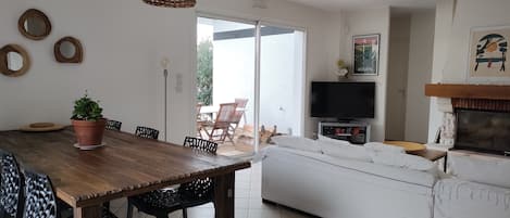 Un coin repas avec une table et des chaises en bois, une plante en pot et un téléviseur en arrière-plan.