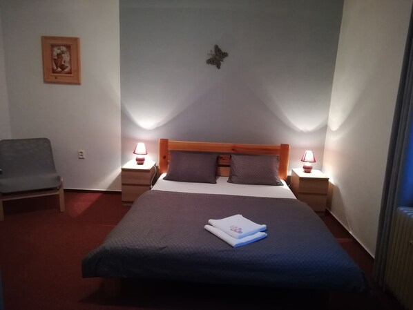 Un dormitorio ordenado con una cama grande, dos mesitas de noche con lámparas, una silla y un cuadro enmarcado en la pared.