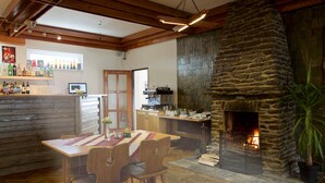 A cozy interior with a stone fireplace, wooden dining table, and a bar area with various bottles. - Hotel Rohanov (Vacov)