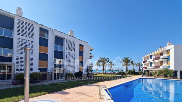 A modern building with a swimming pool, surrounded by palm trees and a clear blue sky.