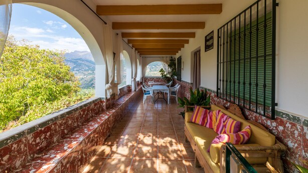 A covered corridor with a bench, a table, and chairs, leading to a view of greenery and mountains. - Jurinea House Lift with private pool (TORRES)