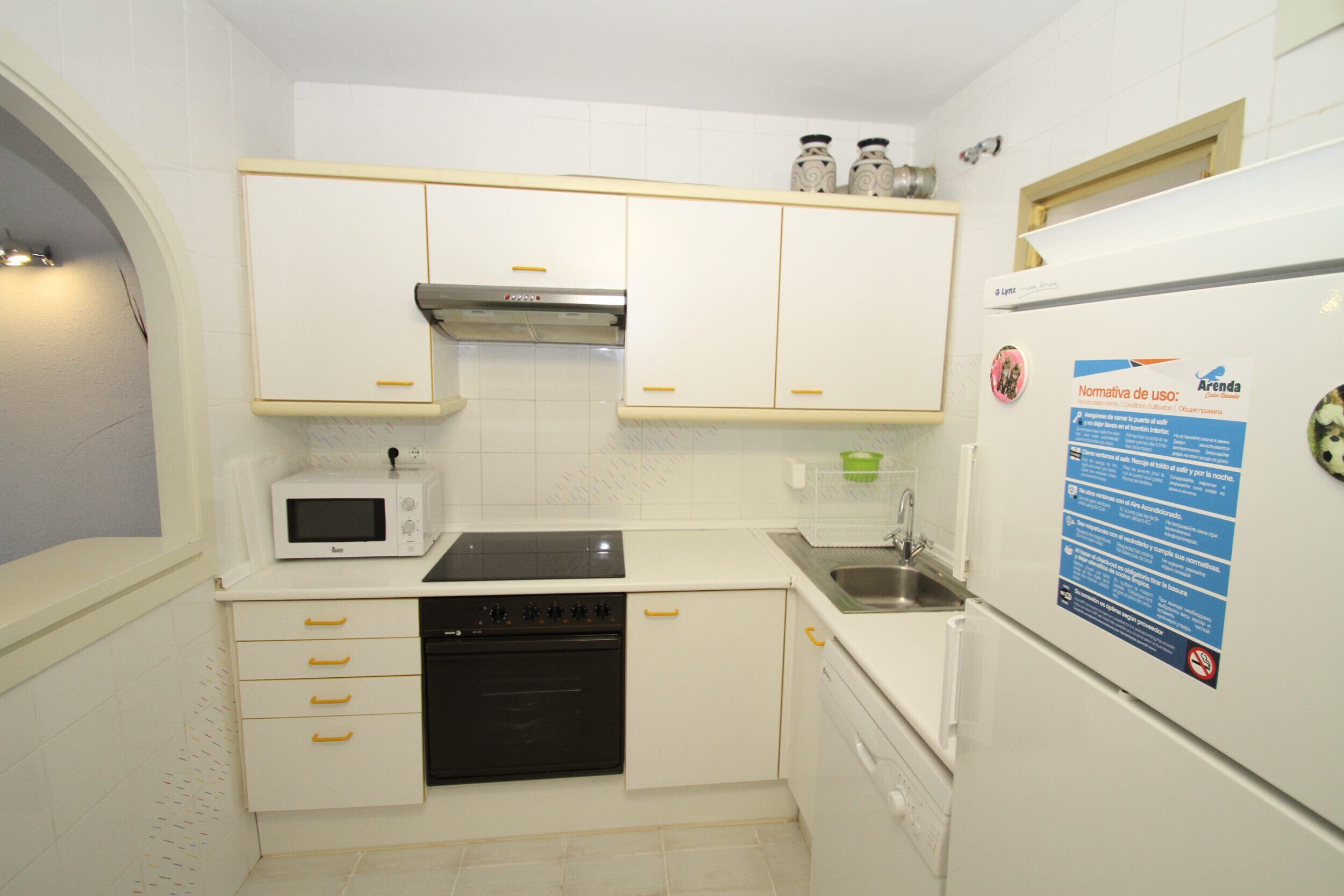 Una cocina compacta con armarios blancos, un microondas, una estufa y un refrigerador.