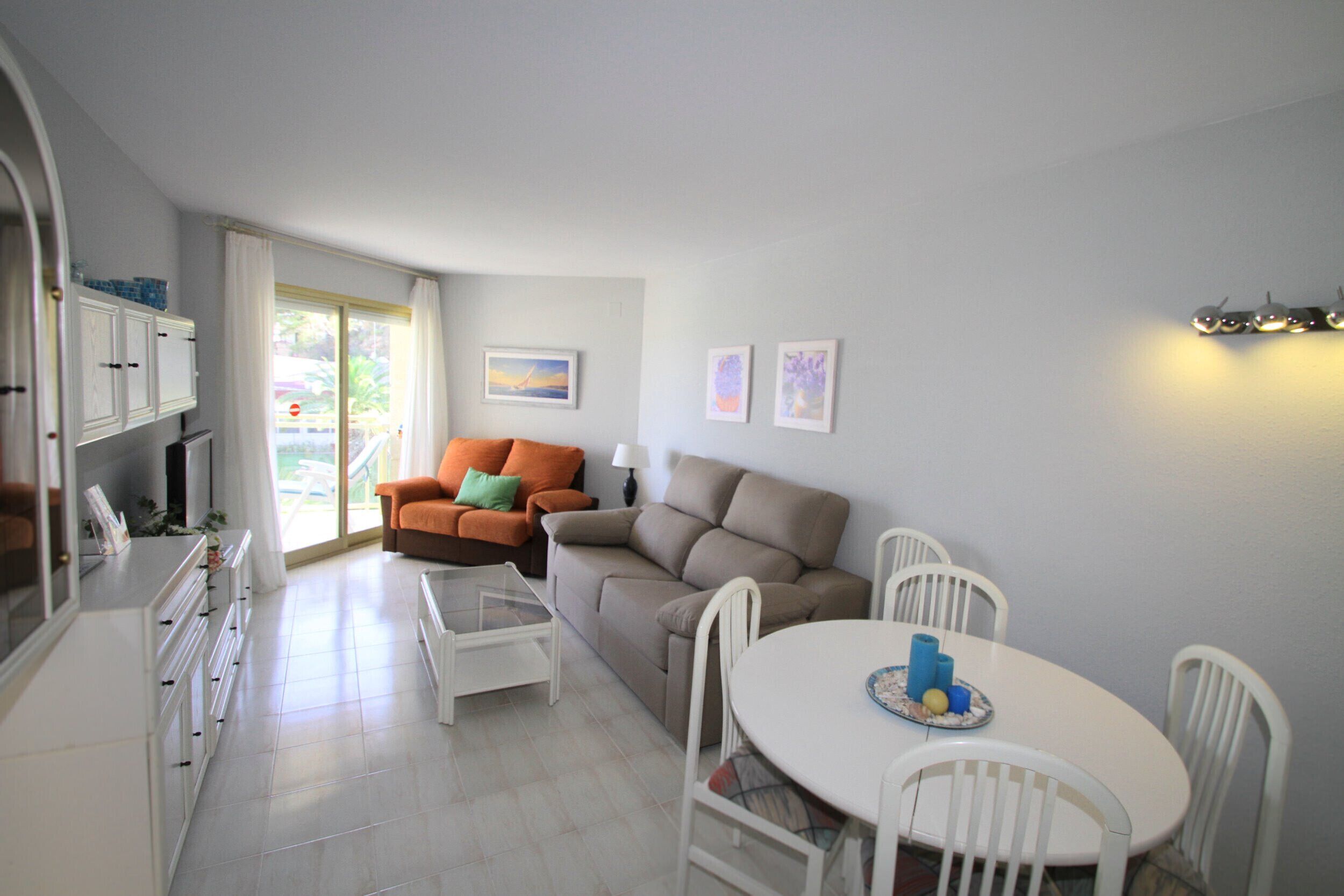 A modern living room with a sofa, a dining table with chairs, and a kitchen area with cabinets and a counter.