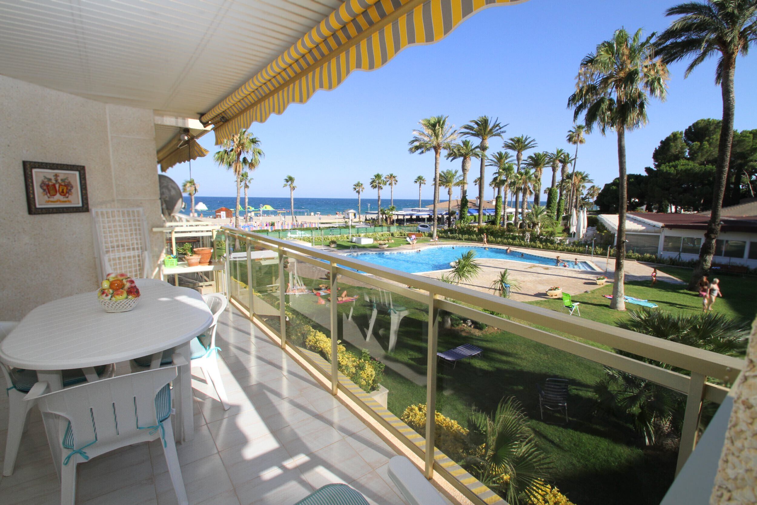 Een balkon met uitzicht op een zwembad, palmbomen en de zee.