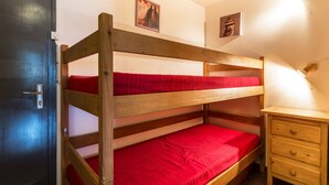 A bunk bed with red bedding, a wooden nightstand, and two wall-mounted pictures. - Cozy studio 4 pers, ski-in/ski-out, terrace, garage, WIFI (La Clusaz)