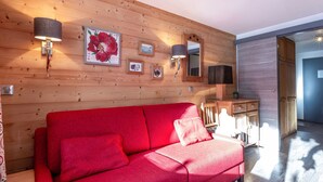 A wooden-paneled room with a red sofa, wall-mounted lamps, framed pictures, and a mirror. - Cozy studio 4 pers, ski-in/ski-out, terrace, garage, WIFI (La Clusaz)