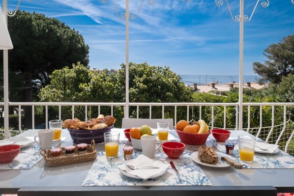 A breakfast table with croissants, fruits, and juice on a balcony overlooking a scenic view.