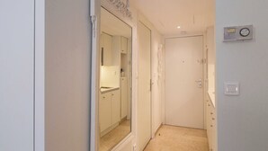 Un couloir étroit, avec une porte au fond, un miroir sur le côté gauche et un thermostat au mur.