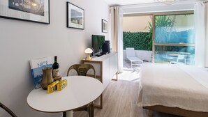 Une chambre d’hôtel moderne équipée d’un lit, d’une table à manger, d’une télévision et d’un balcon offrant une vue sur la verdure.