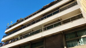 Un immeuble à plusieurs étages, doté de balcons, de grandes fenêtres et surplombant un ciel d’un bleu éclatant.