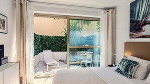 Une chambre d’hôtel comprenant un lit, un bureau, une chaise et une porte vitrée donnant sur un espace extérieur avec une table et des chaises.