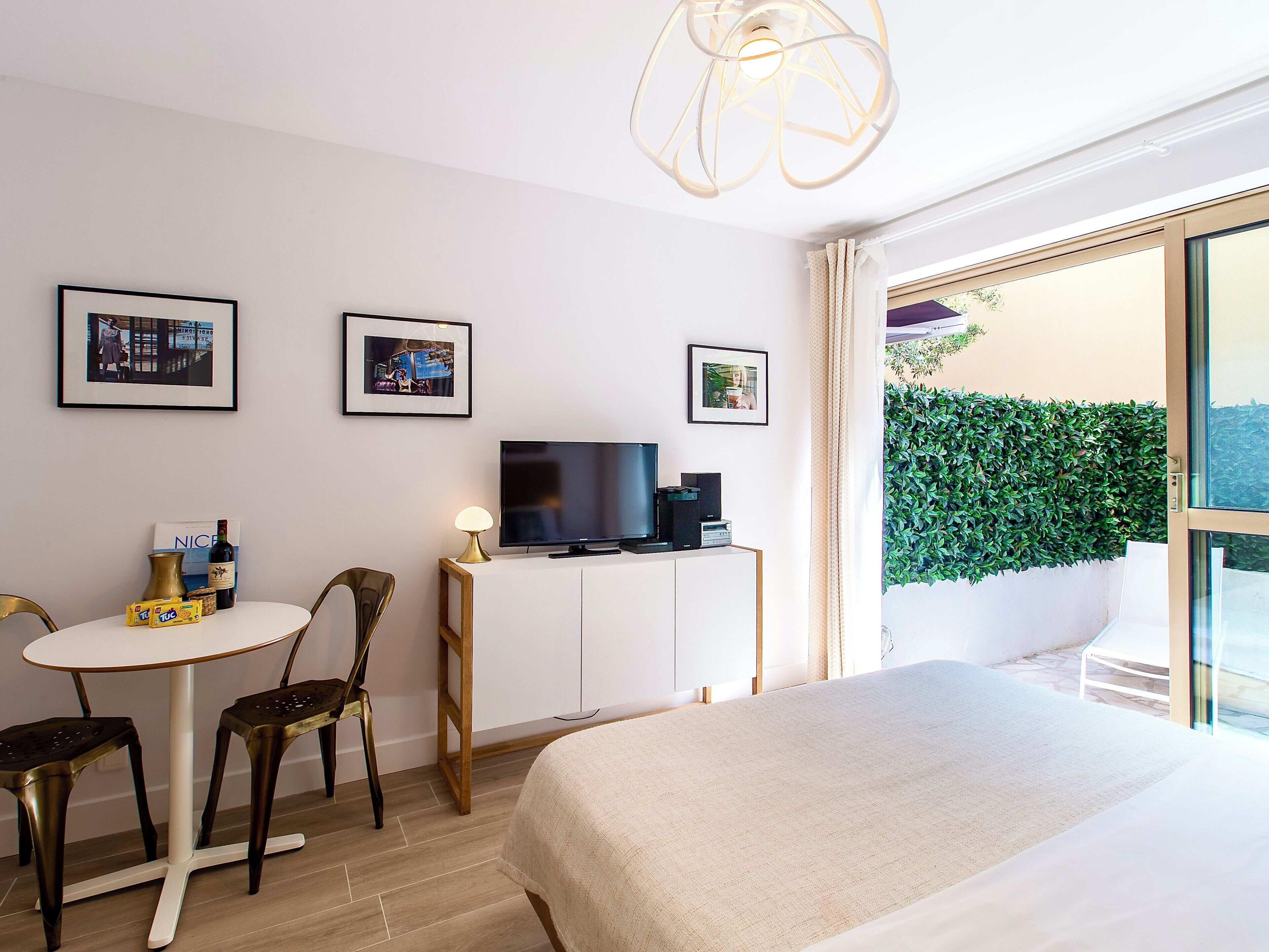 Une chambre d’hôtel avec un lit, une télévision, une petite table avec des chaises et des tableaux encadrés au mur.