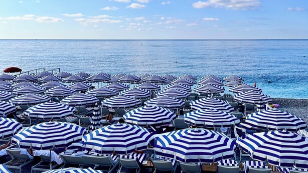 Une plage avec de nombreux parasols et chaises à rayures, un ciel dégagé et une mer calme.