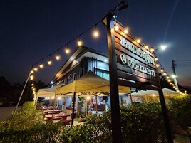 Un edificio con un letrero mostrando un número de teléfono, rodeado de luces colgantes y una zona de estar al aire libre techada.