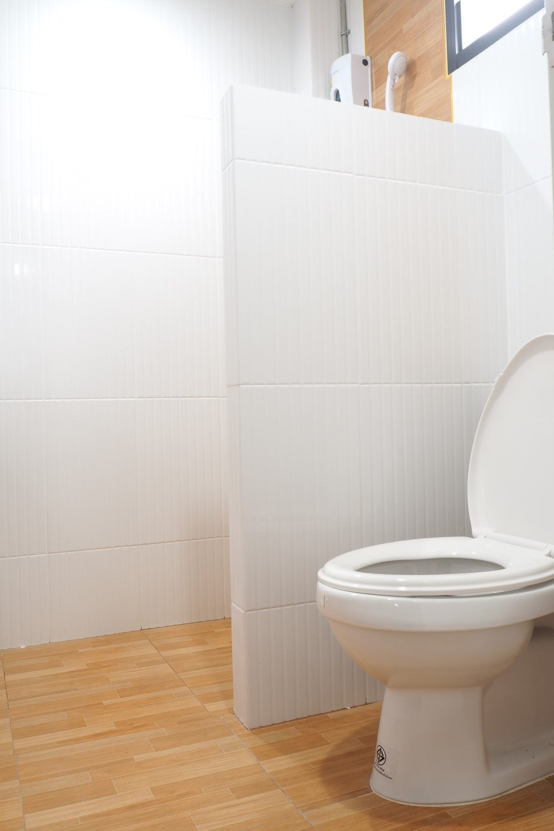 A modern bathroom with a white toilet, wooden flooring, and a white tiled wall.