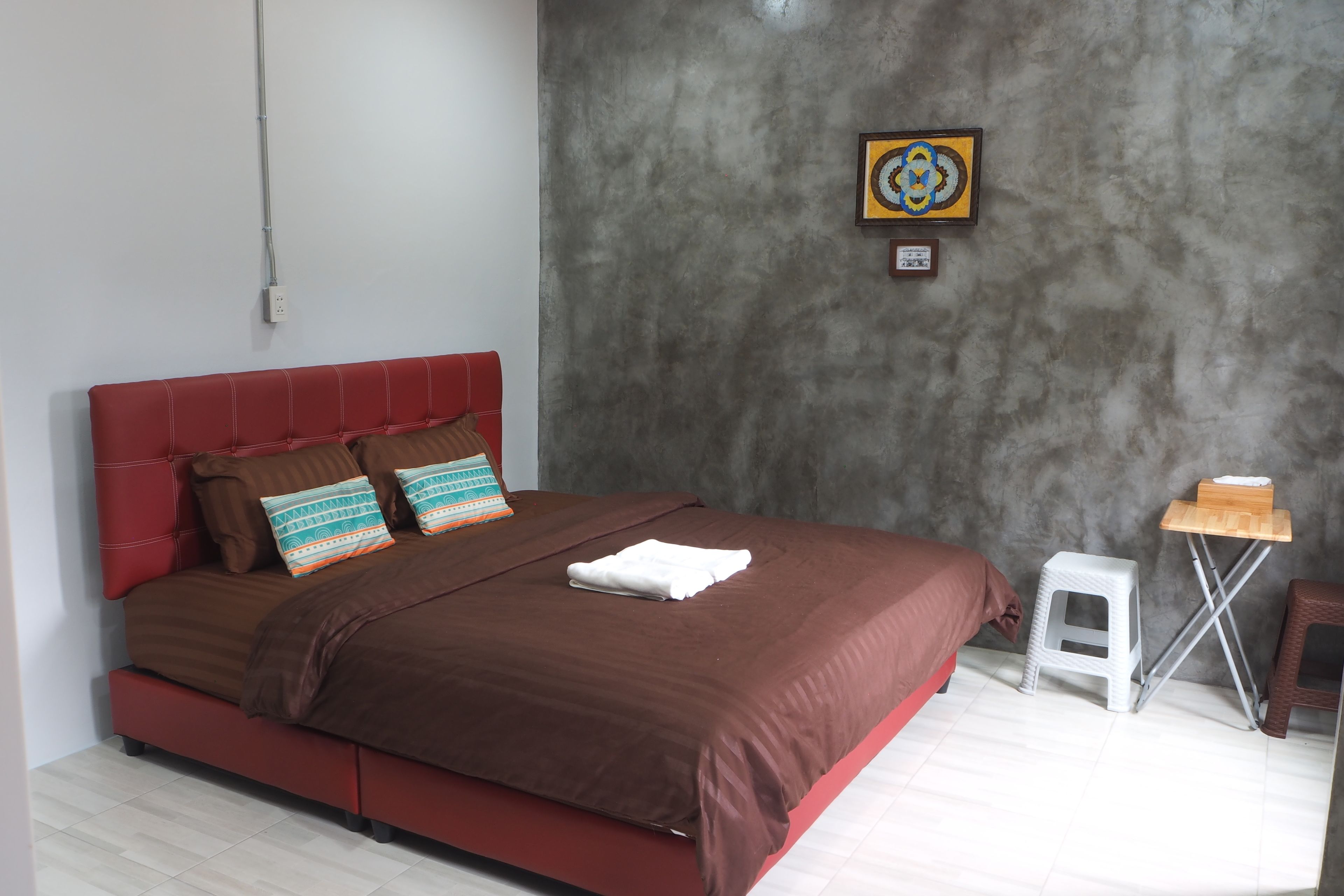 A modern bedroom with a red upholstered headboard, a brown bedspread, and a small white stool.