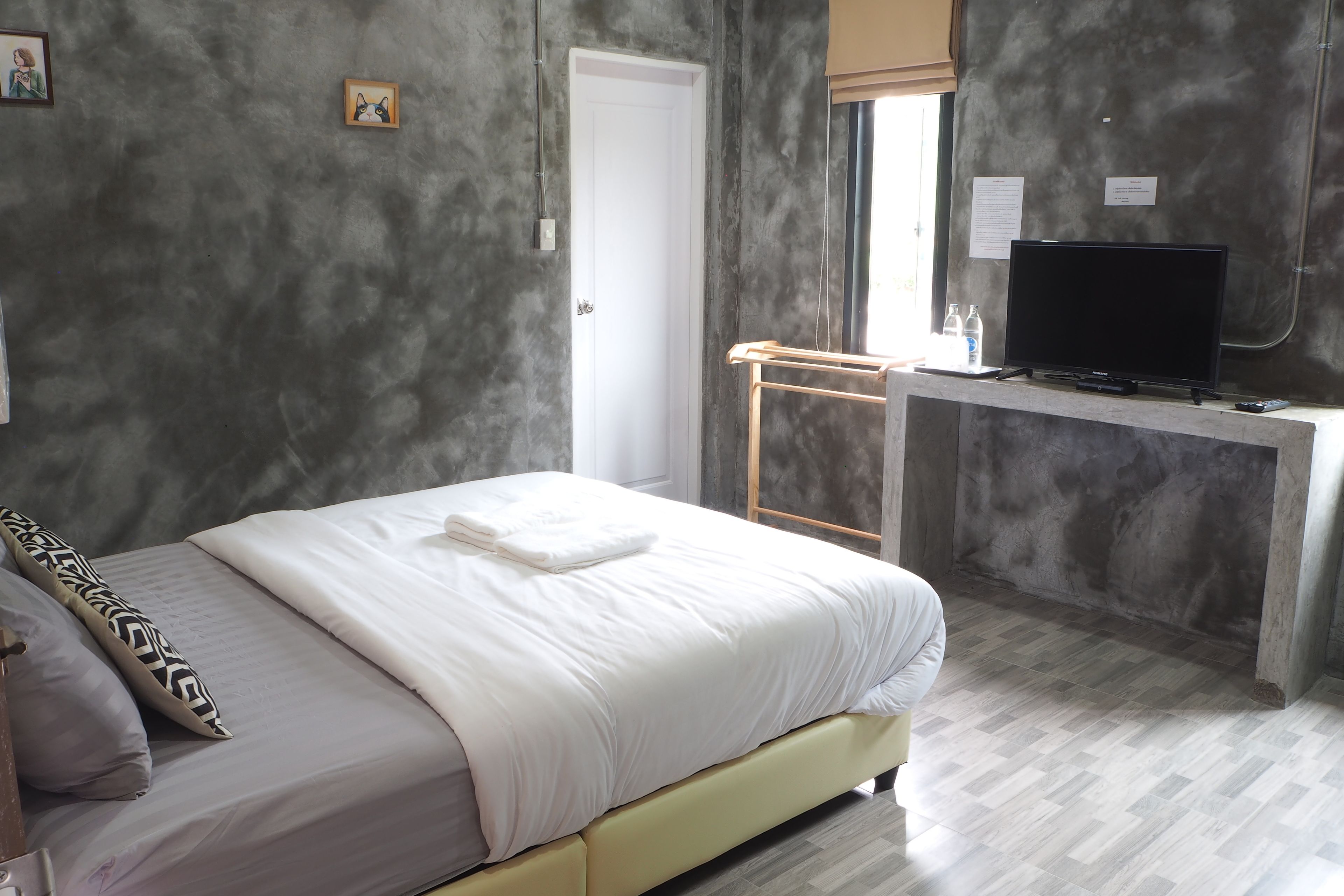 Un dormitorio con cama, televisor sobre un escritorio y ventana con persianas.