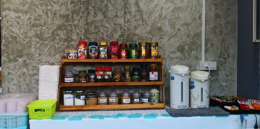 A shelf with various jars and containers, likely containing condiments or preserves, next to a coffee maker and a stack of white plates.