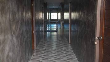 A corridor with dark walls and patterned floor tiles, leading to a bright area with windows.