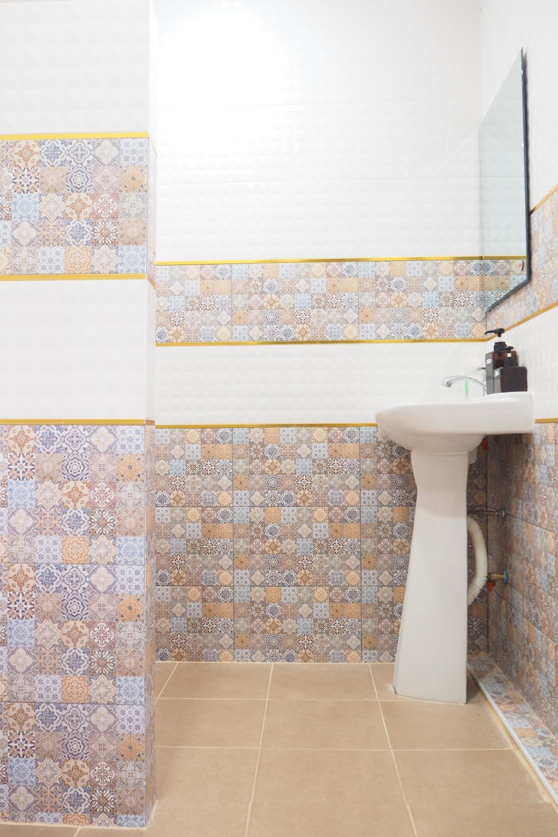 A bathroom with patterned tiles on the walls and floor, a white pedestal sink, and a mirror above the sink.