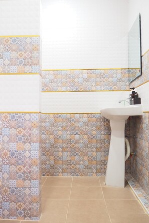 A bathroom with patterned tiles on the walls and floor, a white pedestal sink, and a mirror above the sink. - Ban Kaeng Resort (Chiang Khan)