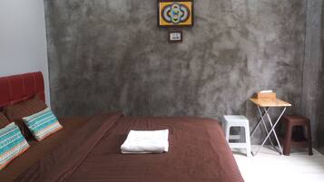 A bedroom with a large bed, a small table, two stools, and a framed picture on the wall.