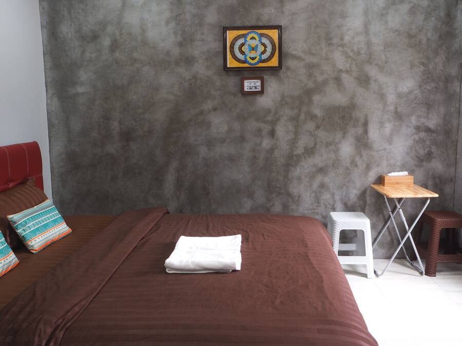 A bedroom with a large bed, a small table, two stools, and a framed picture on the wall.