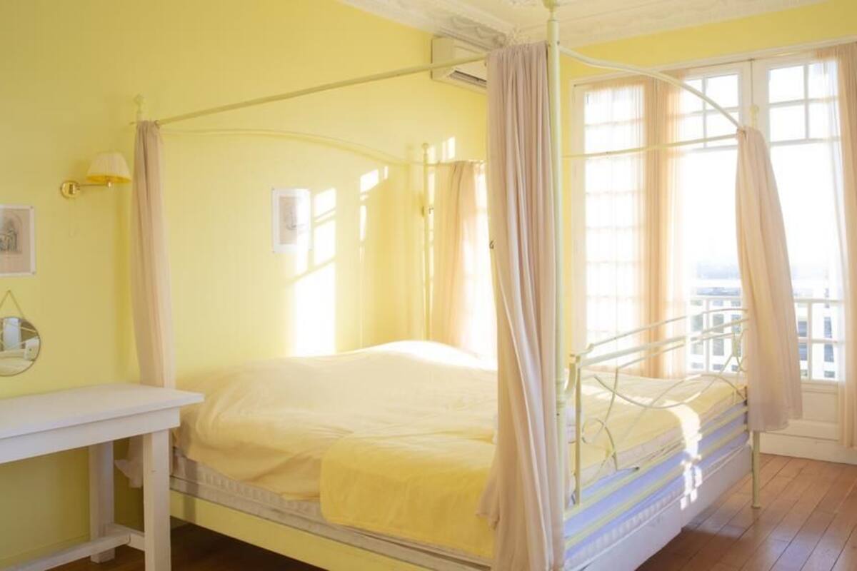 A single bed with a canopy in a room with yellow walls and wooden flooring.