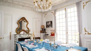 A formal dining room with a marble fireplace, a chandelier, and a large window with curtains. - Villa Ananda Huo (Saint-Cloud)