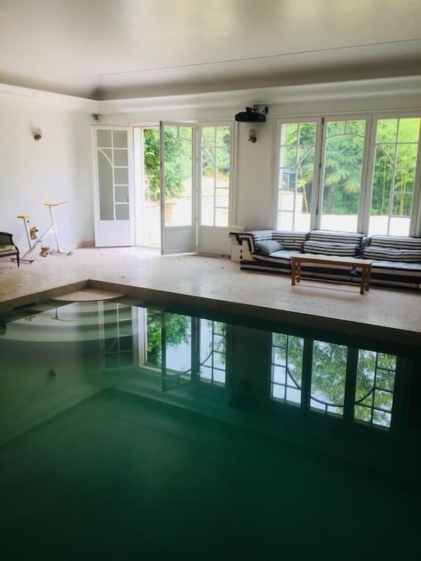 A spacious indoor swimming pool with clear glass walls, a bench, and exercise equipment.