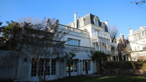 A large, multi-story building with a white facade, multiple balconies, and a prominent staircase leading to the upper levels. - Villa Ananda Huo (Saint-Cloud)