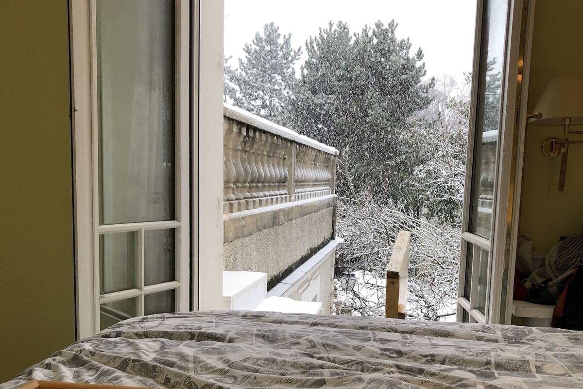 A room with a bed, a window with a view of a snow-covered balcony, and a breakfast tray with a croissant and coffee.