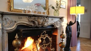 A fireplace with ornate carvings and a lit fire, a golden-framed mirror above it, and a statue to the right. - Villa Ananda Huo (Saint-Cloud)