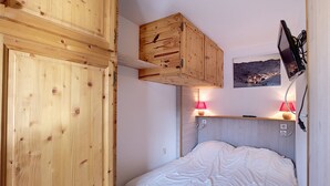 Ein Schlafzimmer mit einem Holzschrank, einem Bett mit weißer Bettwäsche, zwei Nachttischlampen und einem an der Wand befestigten Fernseher.