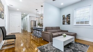 A modern living room with a sofa, coffee table, and a dining area with bar stools. - 15% OFF Monthly | 10% OFF Weekly-Urban Oasis 4BD House close to FQ & City Hot Spots (New Orleans)
