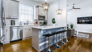 A modern kitchen with white cabinets, a large island with bar stools, stainless steel appliances, and pendant lighting. - 15% OFF Monthly | 10% OFF Weekly-Urban Oasis 4BD House close to FQ & City Hot Spots (New Orleans)