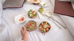 A neatly arranged breakfast spread on a bed with a pillow, a bowl of soup, a salad, a dish of olives, and a tray of bread. - 1920s Boutique Hotel and Restaurants (Cairo)