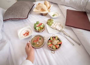 A neatly arranged breakfast spread on a bed with a pillow, a bowl of soup, a salad, a dish of olives, and a tray of bread. - 1920s Boutique Hotel and Restaurants (Cairo)