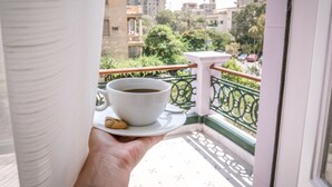A hand holding a cup of coffee with a cookie on a balcony. - 1920s Boutique Hotel and Restaurants (Cairo)