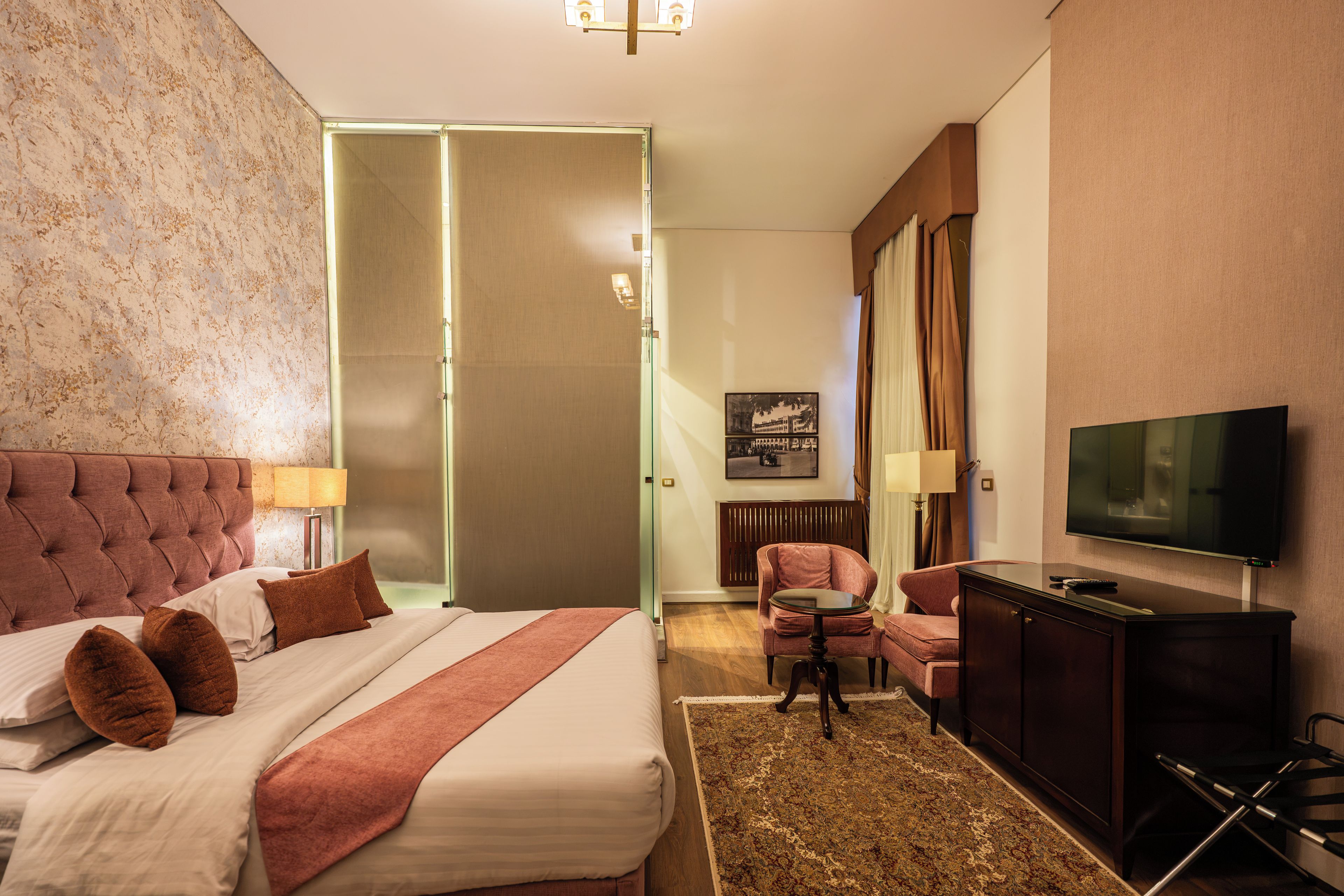 A hotel room with a large bed, a television, a seating area with a chair, and a carpeted floor.