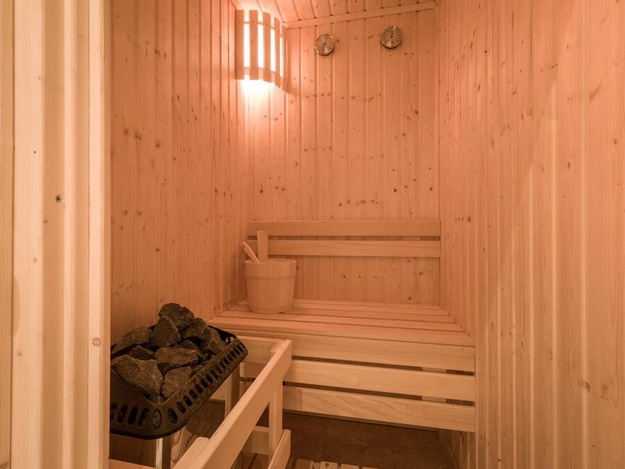 A wooden sauna with benches, a bucket, and a basket of stones.
