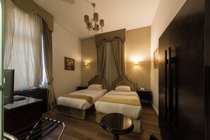 A hotel room with two beds, a desk, a chair, a small table, a television, and a wardrobe.