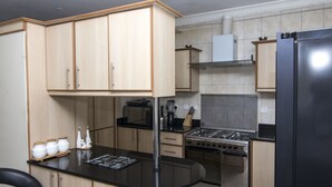 A kitchen with wooden cabinets, a black countertop, a stove, and a refrigerator. - Cozy Nest (Nairobi)