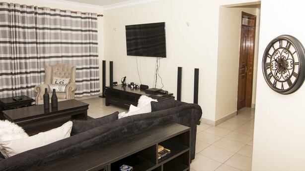 A living room with a sofa, a coffee table, a TV mounted on the wall, and a door leading to another room. - Cozy Nest (Nairobi)