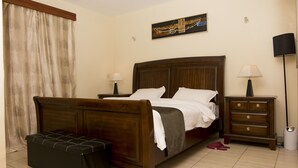 A bedroom with a wooden bed, two bedside tables, a nightstand, a bench, and a painting on the wall. - Cozy Nest (Nairobi)