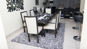 A dining area with a black table, white chairs, and a black and white rug. - Cozy Nest (Nairobi)