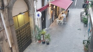 Une ruelle étroite avec un restaurant abrité par un auvent rouge, des tables à l’extérieur et des plantes en pot.