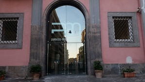 Une entrée d’immeuble avec une grande porte en arc de cercle, deux plantes en pot de chaque côté et une enseigne au-dessus de la porte.
