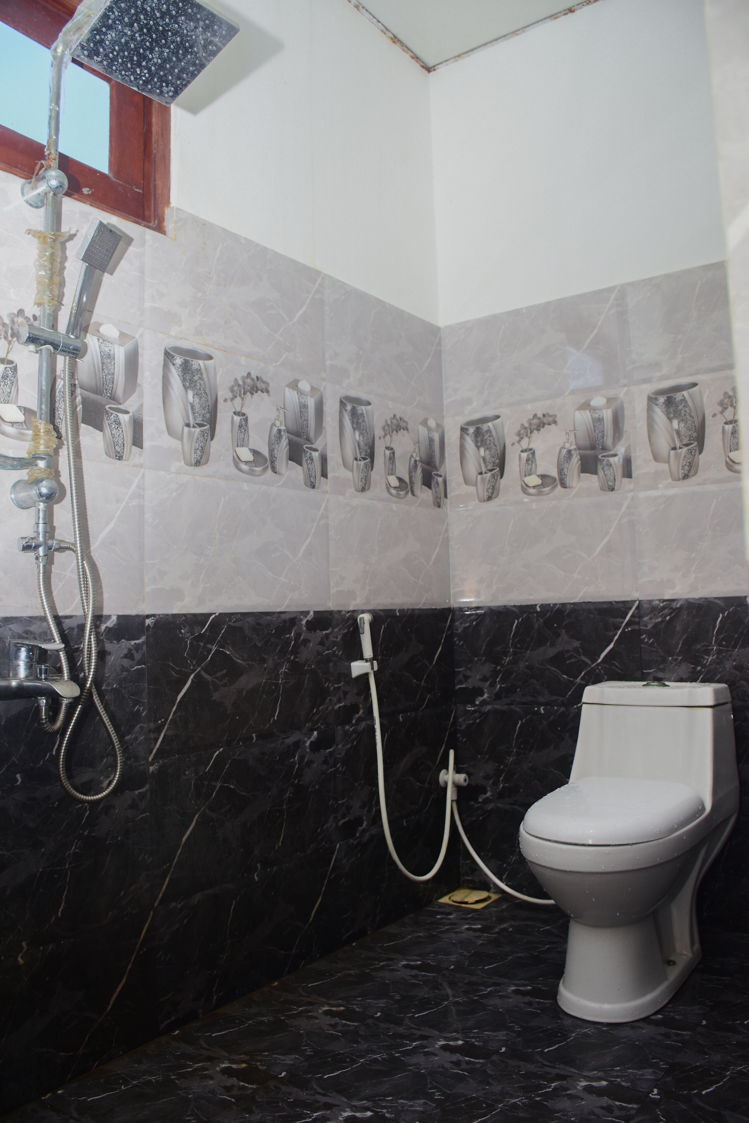 A bathroom with a toilet, a shower, and a marble-tiled wall with decorative vases.